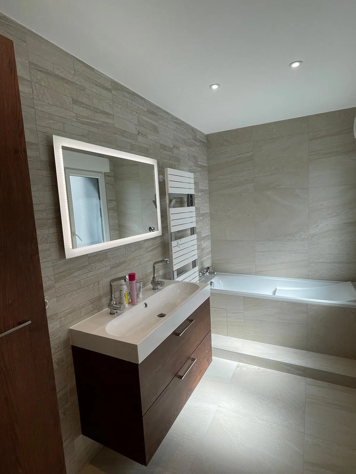 Salle de bains avec baignoire carrelée, meuble vasque suspendu et miroir lumineux
