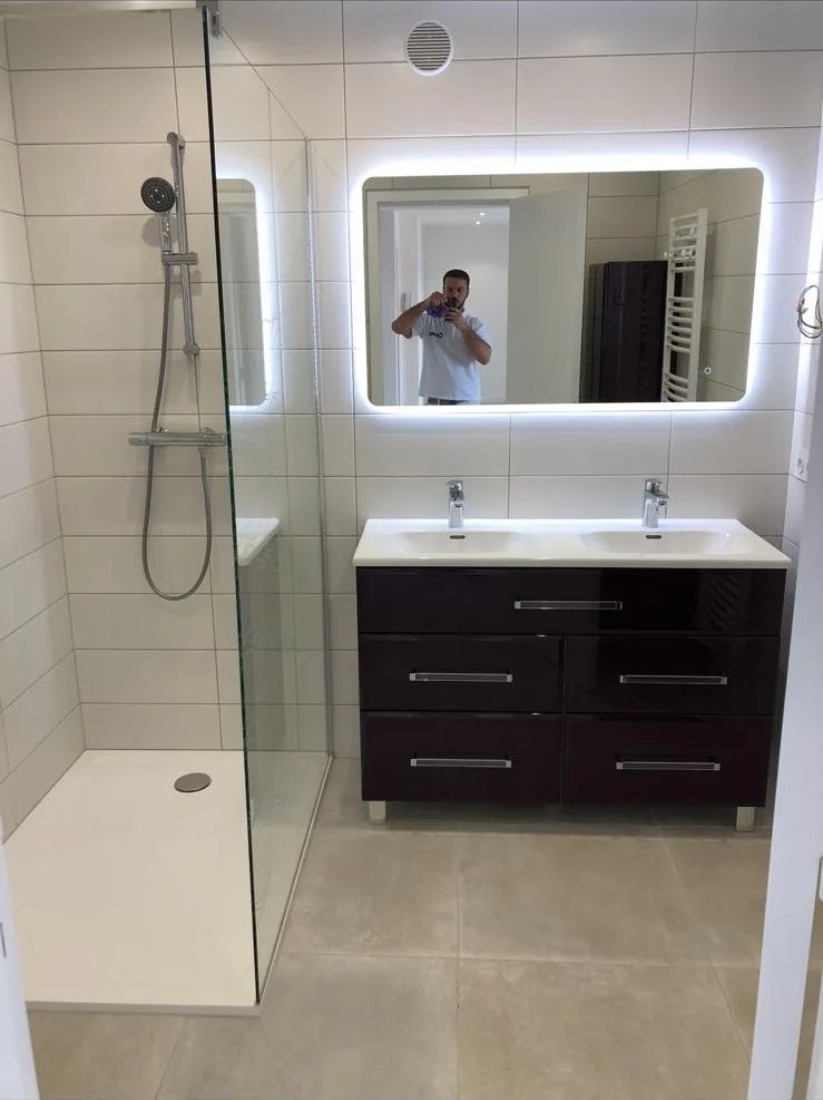 Douche à paroi vitrée et meuble double vasque sous un miroir lumineux