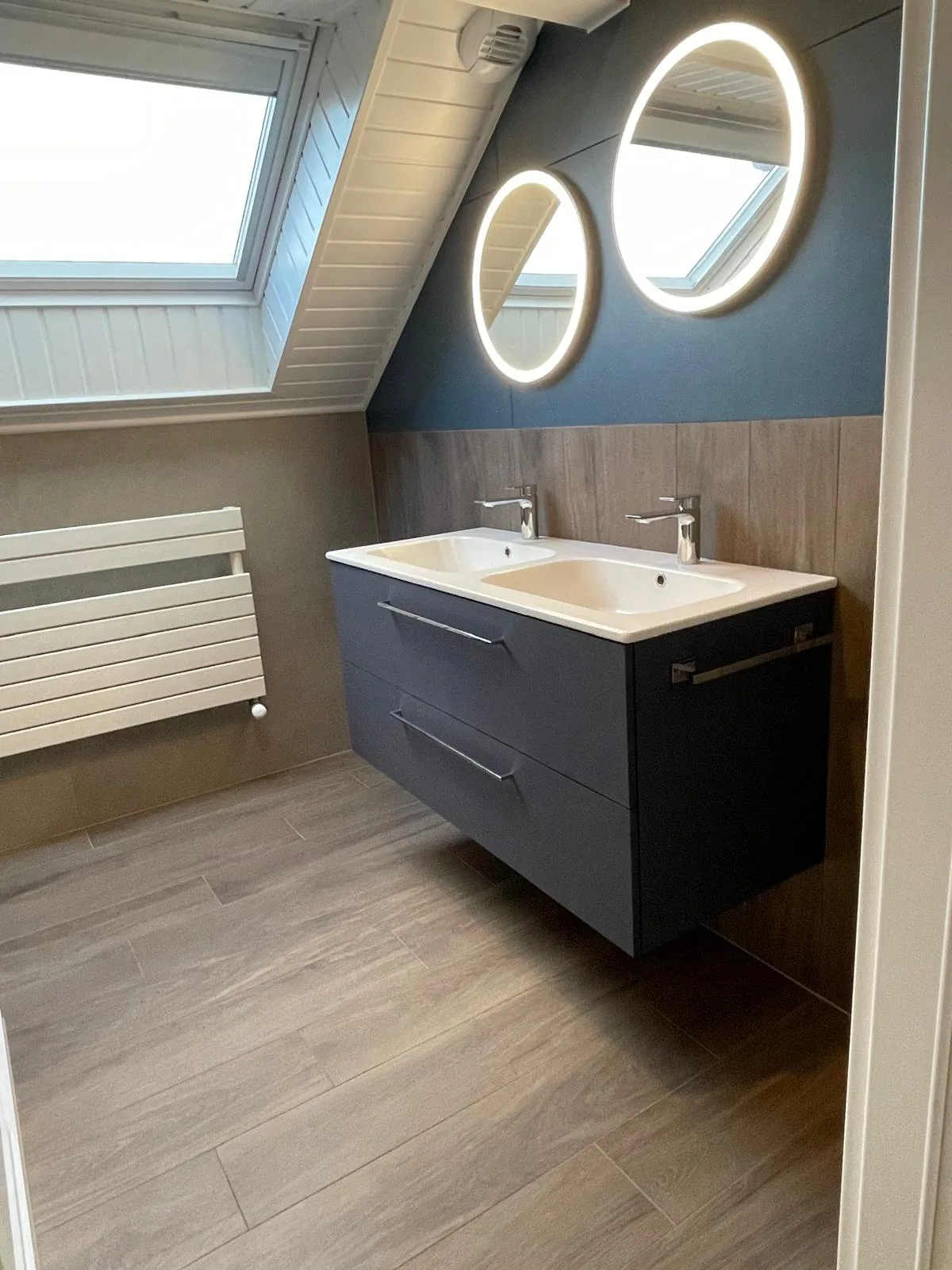 Meuble double vasque gris foncé sous deux miroirs ronds lumineux, devant un mur bleu